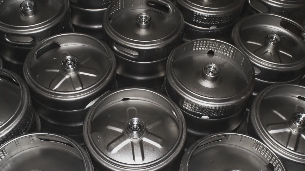 Diversos barris de inox reutilizáveis empilhados, vistos de cima, com acabamento metálico resistente e tampas com válvulas centrais.