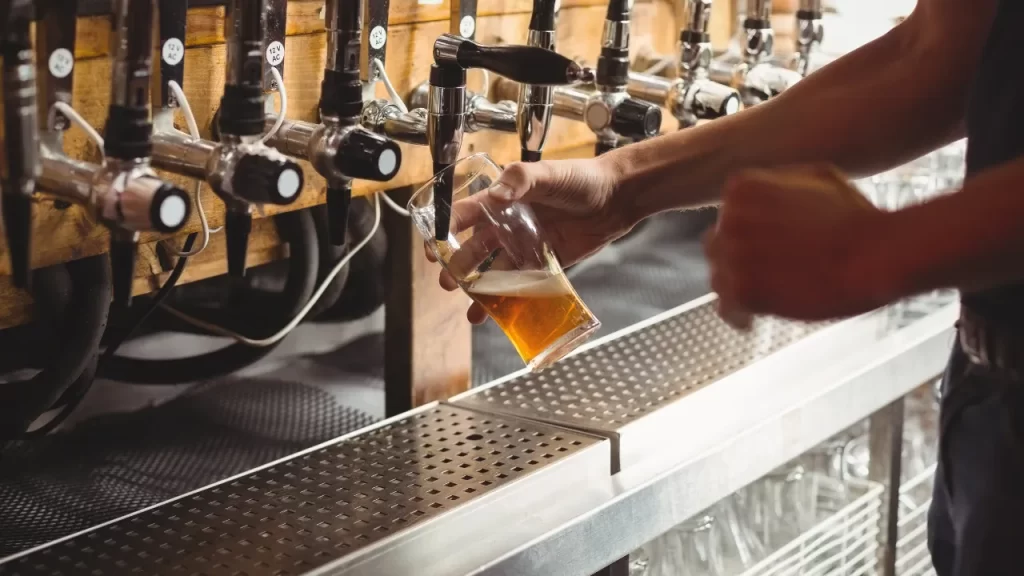 Pessoa servindo cerveja clara em um copo inclinado diretamente de uma torneira em um balcão com várias taps de chope.